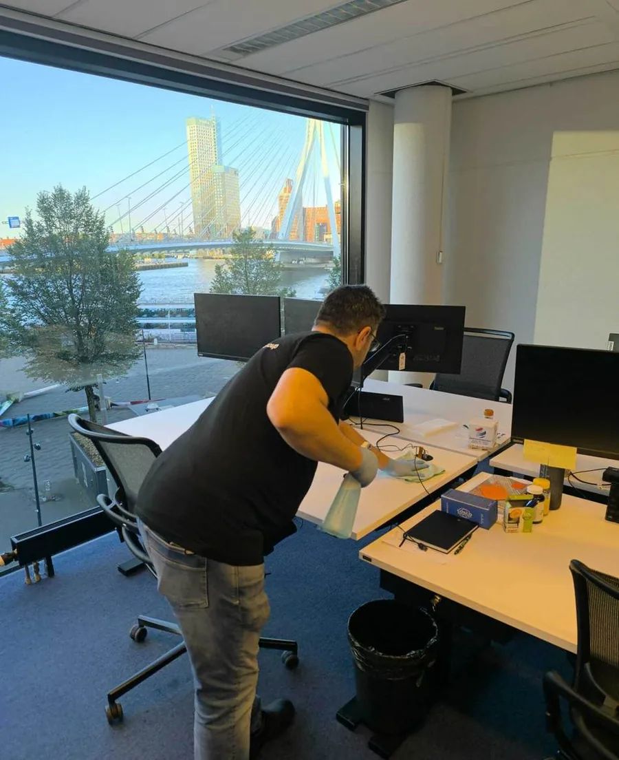 Radix-medewerker maakt een bureau schoon met uitzicht op de Erasmusbrug
